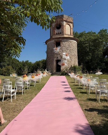 Allée de mariage avec tapis rose et compositions florales devant un moulin en pierre Allée de mariage avec tapis rose et compositions florales devant un moulin en pierre